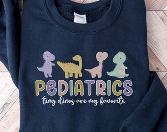 May include: A navy blue sweatshirt with a graphic of four colorful dinosaurs and the text "PEDIATRICS tiny dinos are my favorite".