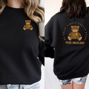 May include: Black sweatshirt with a gold ribbon teddy bear graphic on the front and a gold ribbon teddy bear graphic with the text "No child fights cancer alone. Peds Oncology" on the back.
