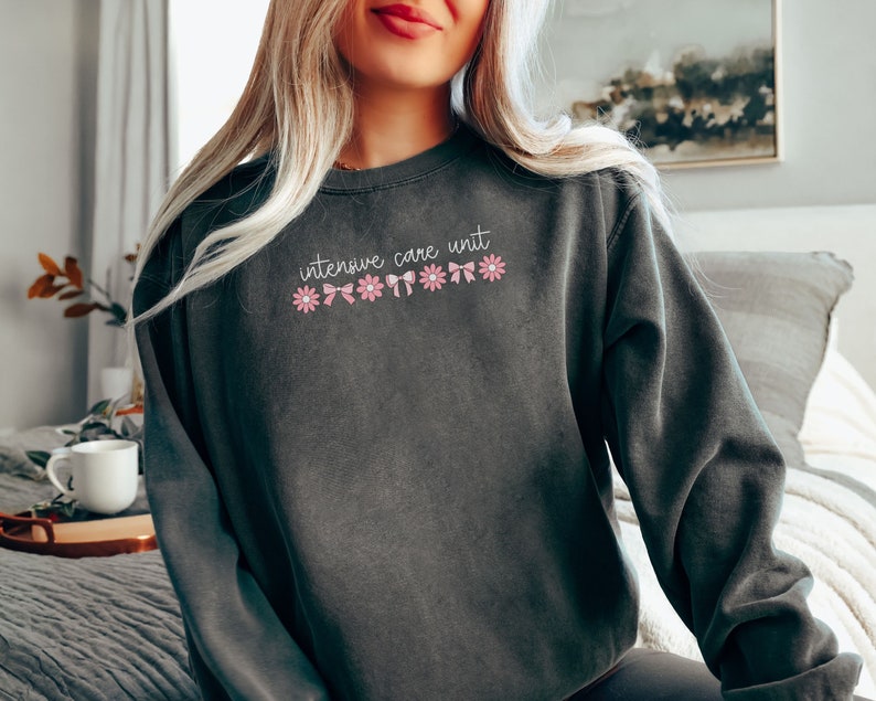 May include: A dark gray sweatshirt with the text "intensive care unit" and pink flowers and bows.