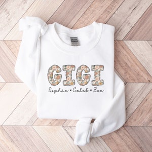 May include: White sweatshirt with a floral print design that spells out "GIGI" and the text "Sophie - Caleb - Zoe" below.