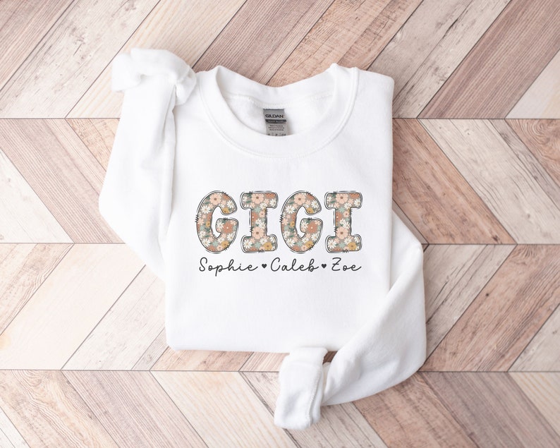 May include: White sweatshirt with a floral print design that spells out "GIGI" and the text "Sophie - Caleb - Zoe" below.