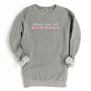 May include: A gray sweatshirt with the text "intensive care unit" in white lettering and a row of pink flowers and bows.