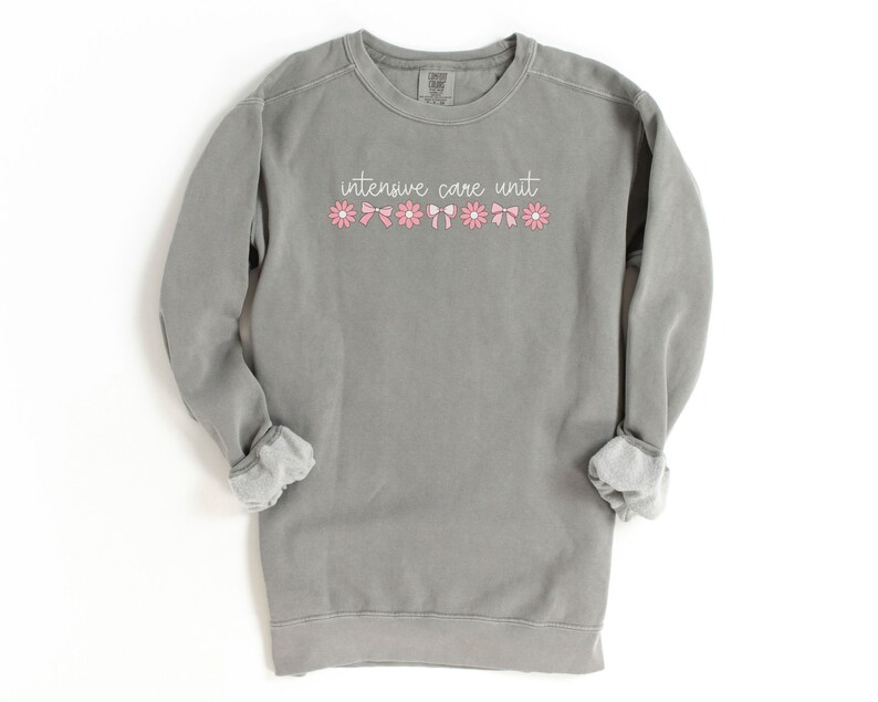 May include: A gray sweatshirt with the text "intensive care unit" in white lettering and a row of pink flowers and bows.
