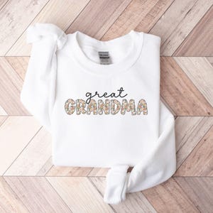 May include: White sweatshirt with the text "great grandma" in black lettering. The letters are decorated with a floral pattern.