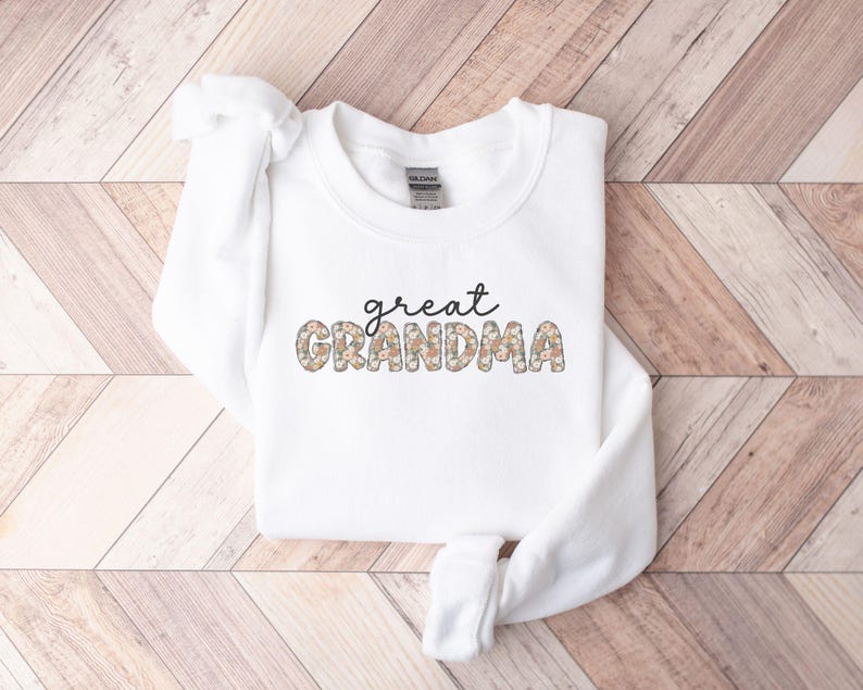 May include: White sweatshirt with the text "great grandma" in black lettering. The letters are decorated with a floral pattern.