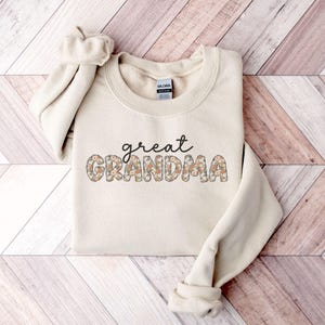 May include: A cream-colored sweatshirt with the text "great grandma" in floral letters.