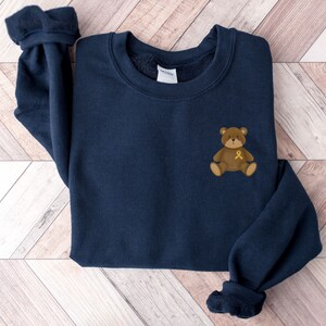 May include: A navy blue sweatshirt with a brown teddy bear wearing a yellow ribbon on its chest.