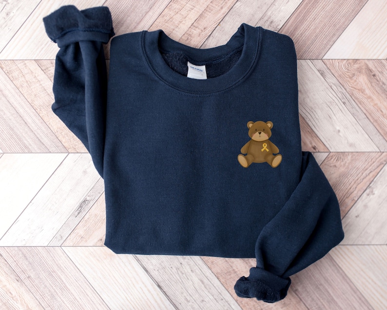 May include: A navy blue sweatshirt with a brown teddy bear wearing a yellow ribbon on its chest.