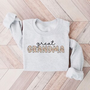 May include: A gray sweatshirt with the text "great grandma" in black lettering with a floral pattern.