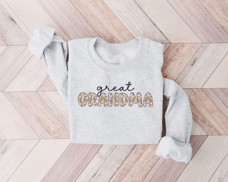 May include: A gray sweatshirt with the text "great grandma" in black lettering with a floral pattern.