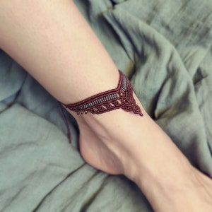 Puede incluir: Un brazalete de tobillo de color marrón y gris con un diseño geométrico y pequeñas cuentas.