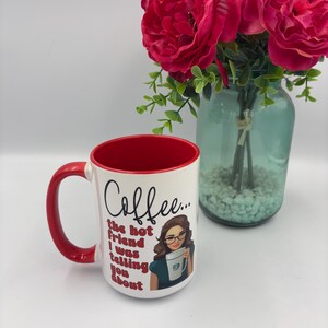 May include: A white ceramic mug with a red interior and handle. The mug features a graphic of a person with brown hair and glasses holding a mug, accompanied by the text: Coffee... the hot friend I was telling you about, written in red script.