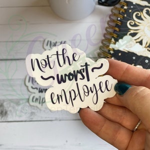 Op de afbeelding: Witte sticker met zwarte tekst die "Niet de ~slechtste~ werknemer" luidt.