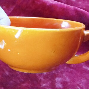 May include: A bright orange ceramic mug with a rounded shape and a handle. The mug is empty and appears to be made of a smooth, glossy material.