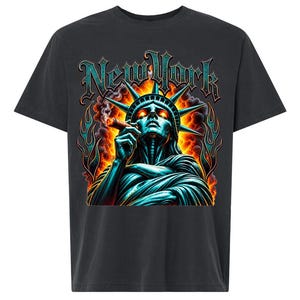 May include: A charcoal gray t-shirt featuring a graphic print of the Statue of Liberty smoking a cigar against a backdrop of orange and yellow flames. The text New York is printed in a stylized teal font above the statue, which has glowing eyes.