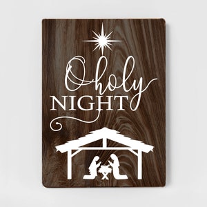 May include: A wooden sign with a brown woodgrain background and white text that reads "O Holy Night". A white silhouette of a manger scene with a star above it is below the text.