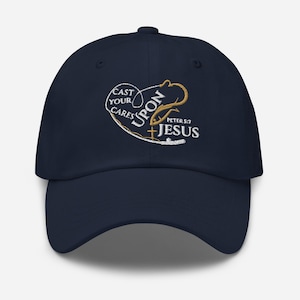 May include: A navy blue baseball cap with an embroidered design that says "Cast your cares upon Jesus" with a fishing hook and fish graphic. The text "Peter 5:7" is also included in the design.