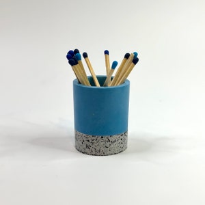 May include: A blue and white speckled ceramic matchstick holder with a group of blue-tipped matches inside.