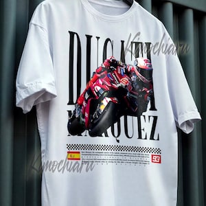 May include: White t-shirt featuring a graphic of a red and black motorcycle with the text "DUCATI MARQUEZ" in large black letters. Includes the number "93" and a Spanish flag.