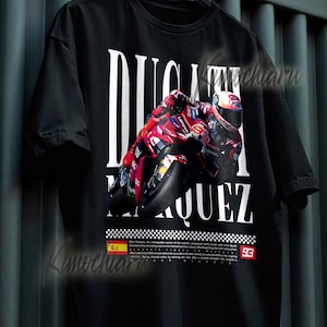 May include: Black t-shirt featuring a motorcycle racing design with the words "DUCATI MARQUEZ" in white. The graphic includes a red and black motorcycle and the number 93. The shirt is hanging on a black hanger.
