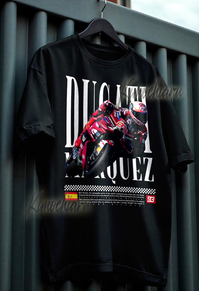 May include: Black t-shirt featuring a motorcycle racing design with the words "DUCATI MARQUEZ" in white. The graphic includes a red and black motorcycle and the number 93. The shirt is hanging on a black hanger.