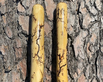 May include: Two wooden sticks with a unique, natural, lightning-like pattern. The sticks are light brown with dark brown markings.