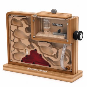 May include: A tan-colored ant farm with a clear viewing area, featuring a sand-filled chamber and a network of tunnels. The text "Expanse" is visible on the clear section. The base of the farm has the text "Antopia Nests".
