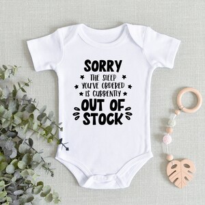 May include: White baby onesie with black text that reads "SORRY * THE SLEEP * YOU'VE ORDERED * IS CURRENTLY * OUT OF STOCK".