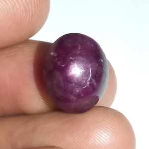 May include: A deep red oval-shaped gemstone with a smooth, polished surface. The gemstone has a slight sparkle and is set against a white background.