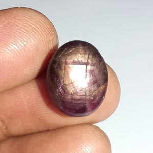 May include: A close-up of a red star ruby gemstone with a cabochon cut. The ruby has a star-like pattern with a silvery sheen.