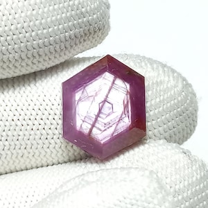 May include: A pink hexagonal ruby gemstone with a star-like pattern inside.