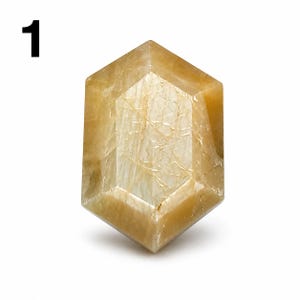 May include: A faceted, hexagonal-shaped gemstone with a translucent, golden-brown hue. The stone features internal veining and a polished surface that reflects light across its multiple angled planes, showcasing a warm, earthy, amber-like color profile.