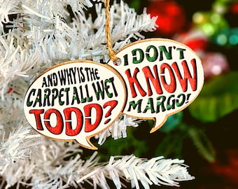 May include: Two Christmas decorations with a white background and green and red lettering. One decoration says "And why is the carpet all wet Todd?" and the other says "I don't know Margo!"