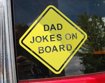 May include: A yellow diamond-shaped sticker with a black border and the words "DAD JOKES ON BOARD" in black text. The sticker is affixed to a car window, with a red car bumper visible.