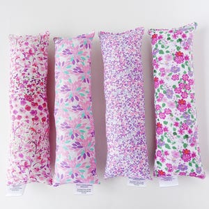 May include: Four long, rectangular pillows with different floral patterns. The pillows are made of a soft, white fabric with pink, purple, and green floral designs.