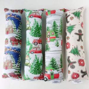 May include: Four long, rectangular catnip toys with different Christmas-themed patterns. The toys are made of fabric and have a white background. The patterns include a red car, a green camper, a gingerbread man, and a house with a snowman.