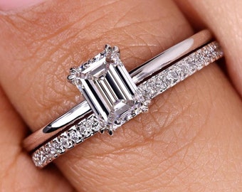 Op de afbeelding: Een close-up van een zilveren verlovingsring met een vierkante smaragd geslepen diamant. De ring is bezet met kleinere diamanten op de band.