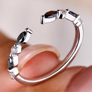 May include: A silver ring with a row of black and white marquise-shaped stones. The ring is open on one side, making it adjustable.