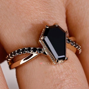 Può includere: Un anello d'oro con una pietra preziosa nera a forma di bara e accenti di diamanti neri.