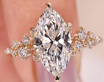 Könnte beinhalten: Ein goldener Ring mit einem großen, marquiseförmigen Diamanten im Zentrum. Der Diamant ist von kleineren, runden Diamanten in einem floralen Design umgeben. Der Ring hat ein poliertes Goldband.