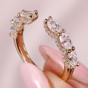 Puede incluir: Un anillo dorado con un diseño abierto, con múltiples piedras preciosas de corte ovalado. El anillo está adornado con piedras más pequeñas y brillantes alrededor de las gemas más grandes, creando una apariencia lujosa y elegante.