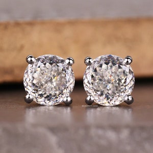 May include: A pair of silver stud earrings with round, clear, faceted gemstones.