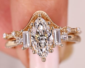 May include: A gold engagement ring featuring a marquise-cut diamond centre stone, with two baguette-cut diamonds either side. The ring has an intricate design with smaller diamonds and a matching band. The ring is set in a gold band.