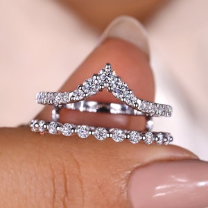 May include: A delicate, two-piece wedding ring set with a curved, v-shaped band and a smaller, round band, both adorned with sparkling diamonds.