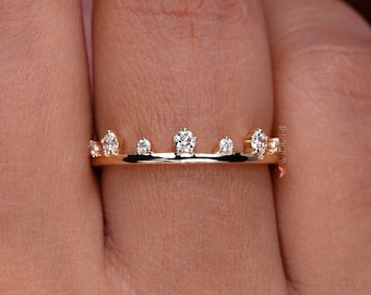 May include: A delicate gold ring featuring a series of small, sparkling diamonds. The ring's design is a repeating pattern of diamonds, creating a crown-like appearance. The ring is shown on a finger, highlighting its elegant and refined style.