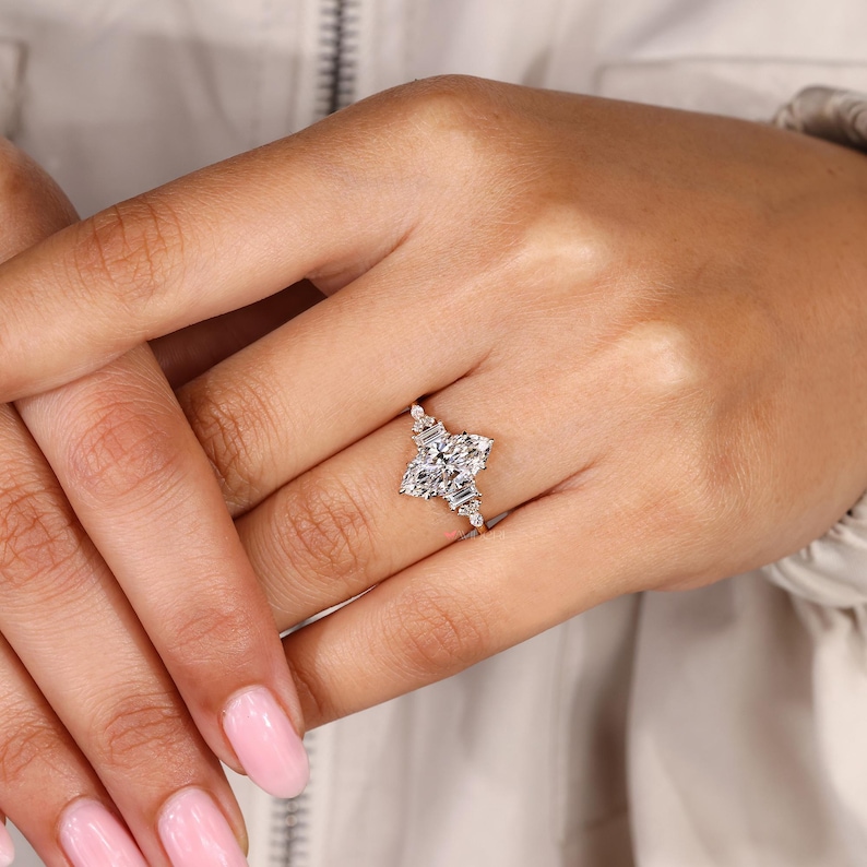 May include: A diamond engagement ring featuring a cluster of rectangular and square-cut stones. The ring's design includes a central square-cut diamond surrounded by smaller, rectangular diamonds, set on a delicate band. The ring is shown on a person's finger.
