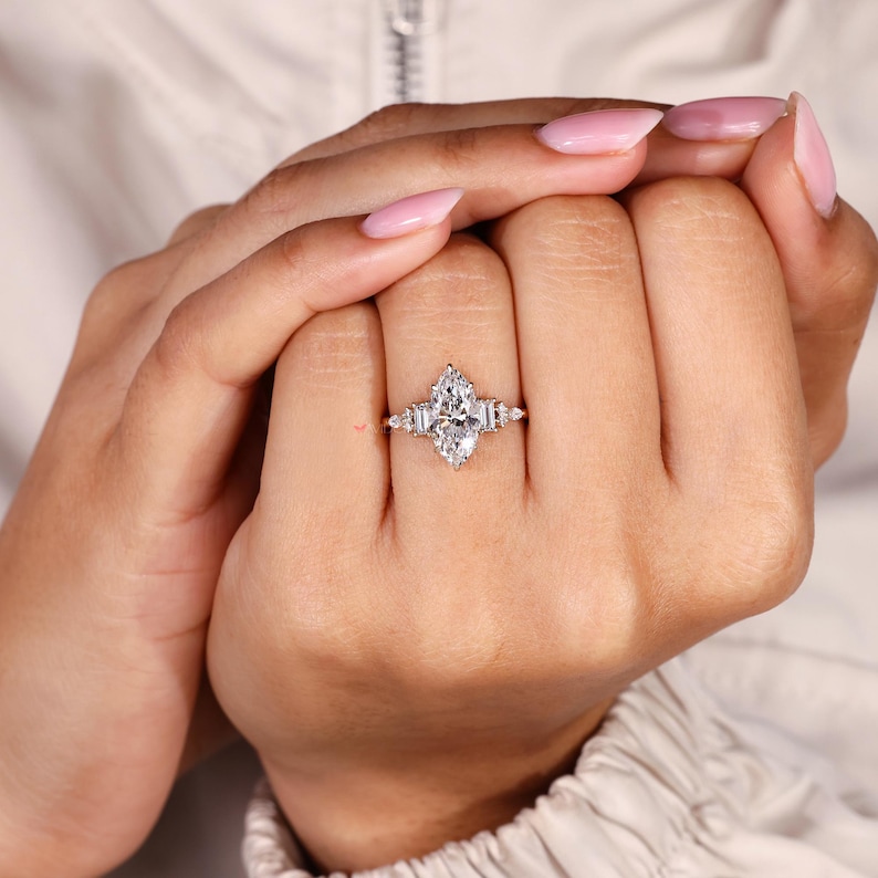 May include: A marquise-cut diamond ring with baguette side stones. The ring features a large, central diamond with a pear-like shape, flanked by smaller, rectangular diamonds. The ring is set on a delicate band, showcasing the sparkling stones.