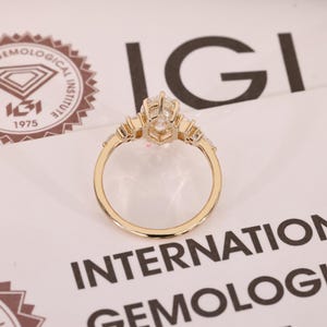 May include: A gold ring with a large, clear, faceted center stone and smaller stones on either side. The ring is set against a white background with the text "IGI INTERNATIONAL GEMOLOGICAL INSTITUTE".