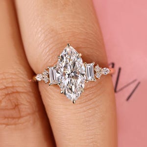 May include: A marquise-cut diamond engagement ring with a gold band. The ring features a large, central marquise diamond, flanked by two smaller emerald-cut diamonds and several smaller accent stones.