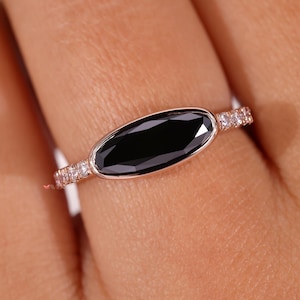 May include: A rose gold ring with a black oval gemstone and a band of small white diamonds.
